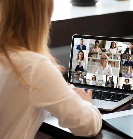 A female employee participates in a virtual team meeting with colleagues on a laptop.