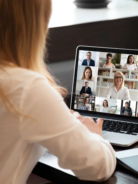 A female employee participates in a virtual team meeting with colleagues on a laptop.