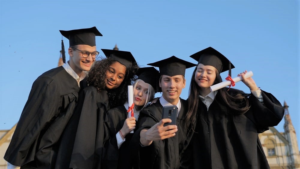 A group of university students in graduation gowns and caps taking a selfie together.