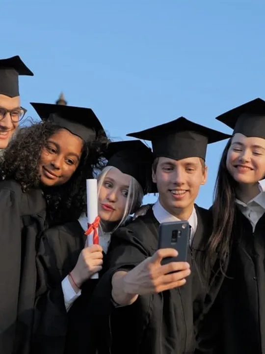 A group of university students in graduation gowns and caps taking a selfie together.