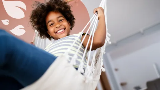 Happy child relaxing in a hammock at home, smiling confidently at the camera.
