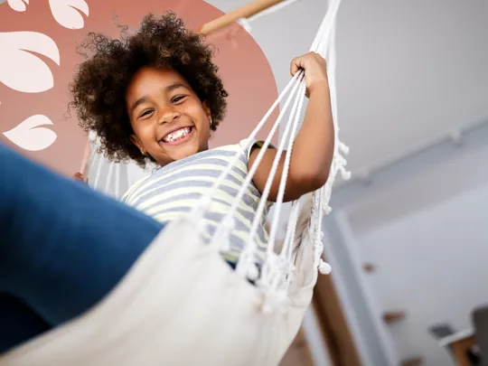 Happy child relaxing in a hammock at home, smiling confidently at the camera.