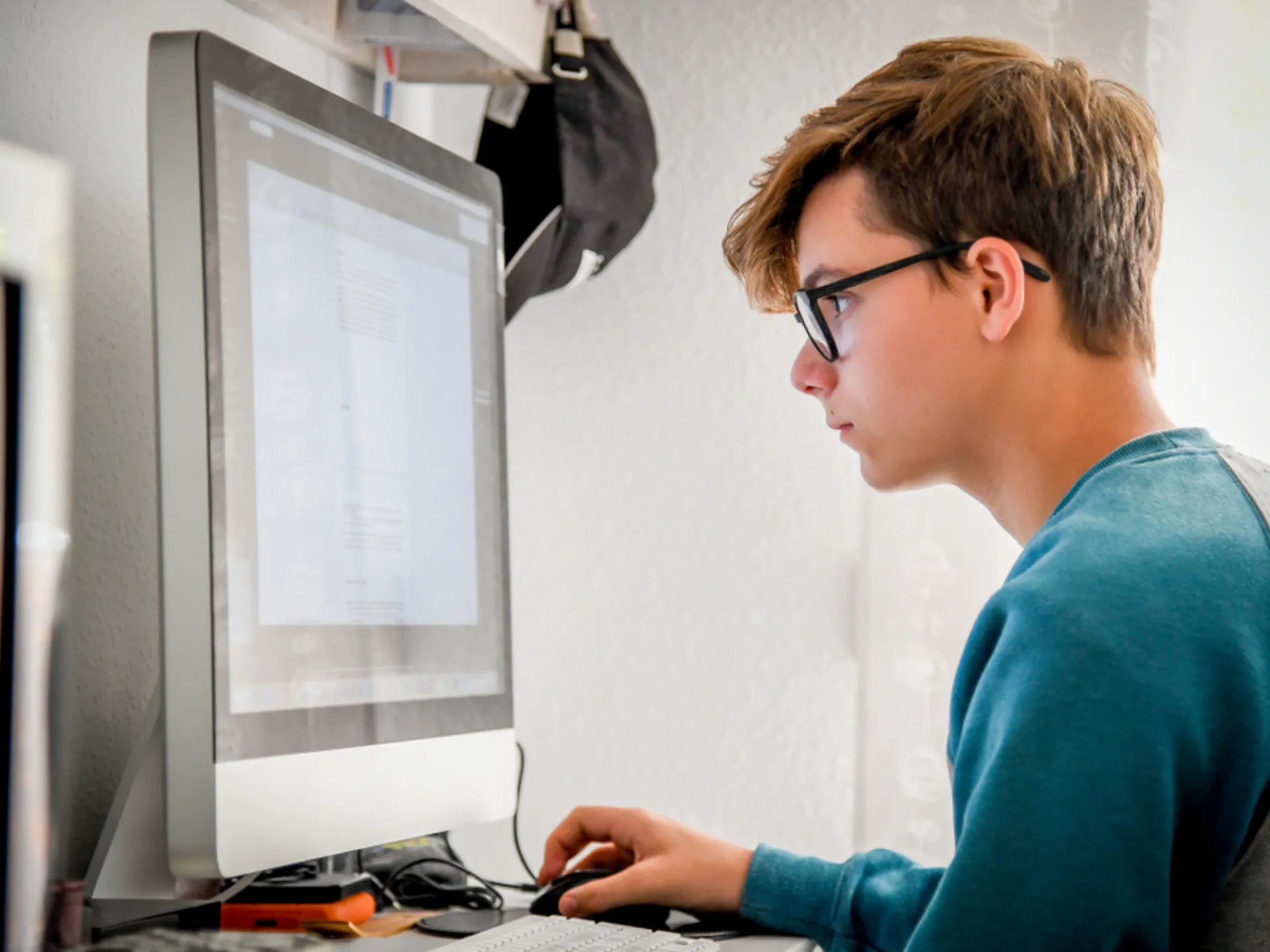 Focused teenage boy using a desktop computer for study or research in a home learning space.