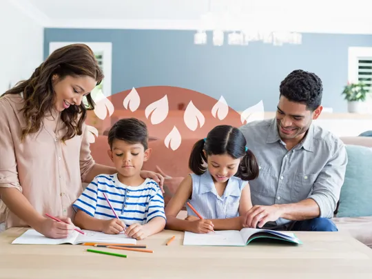 Two parents supporting their young children with schoolwork around a living room table.