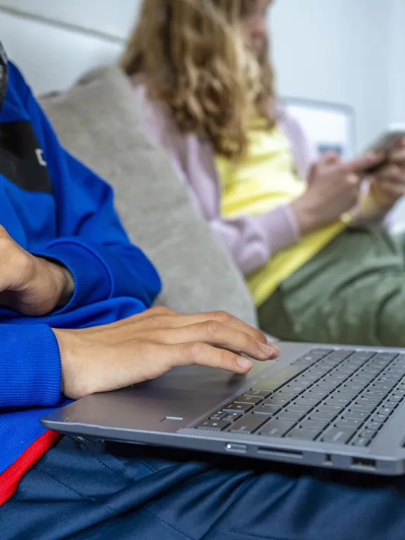 Close-up of a student using a laptop with headphones around their neck, representing responsible digital learning and online safety at Pamoja.