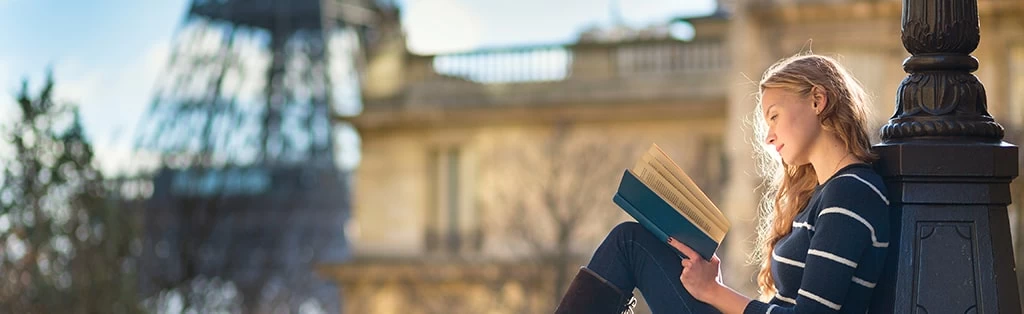 A woman reading a book in view of the Eiffel Tower. 