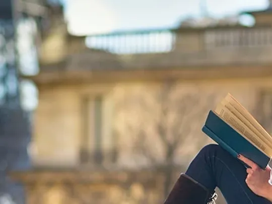 A woman reading a book in view of the Eiffel Tower.