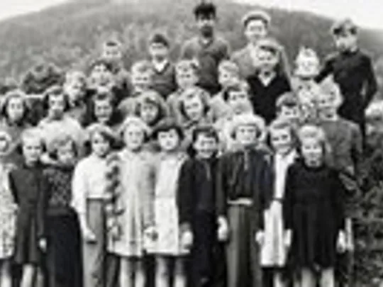 An old black and white photograph of a group of schoolchildren standing together and looking at the camera.