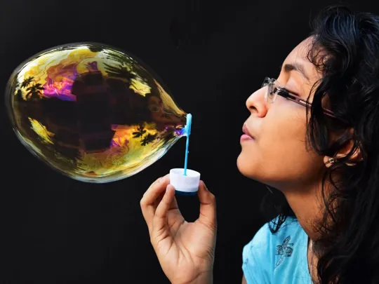 A girl blowing a bubble through a plastic hoop.