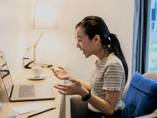 A young girl studying on her laptop at her desk.