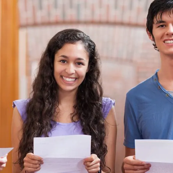 Students standing together, smiling and holding their exam result sheets.