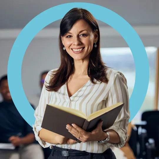 A teacher standing with a notebook, looking at the camera.
