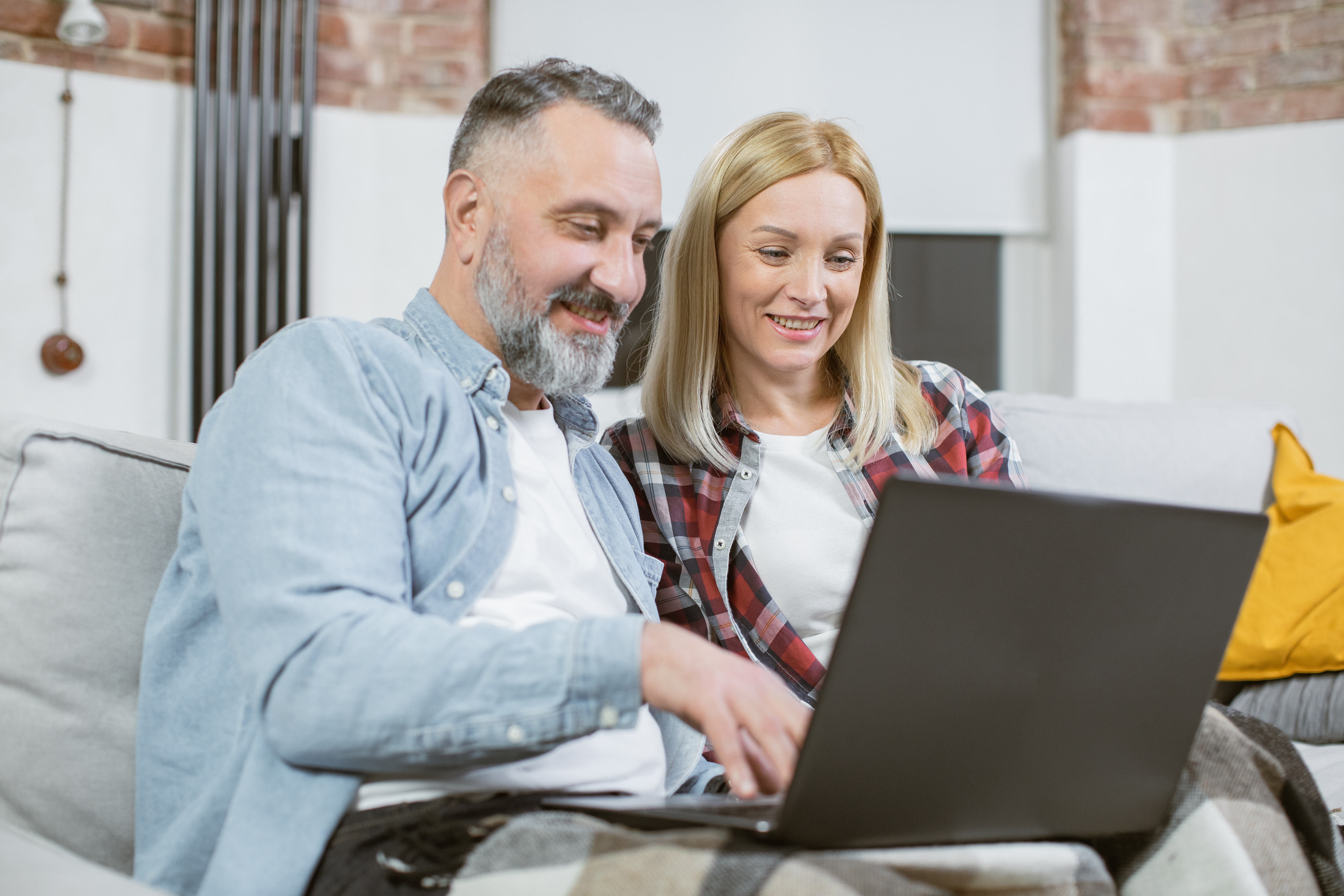 Smiling couple using a laptop together in a cosy home environment.