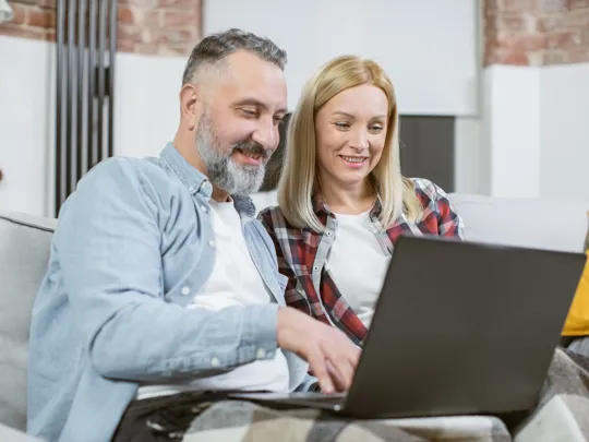 Smiling couple using a laptop together in a cosy home environment.