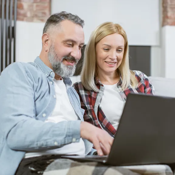 Smiling couple using a laptop together in a cosy home environment.