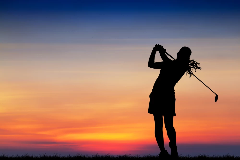 A silhouette of a golfer completing a swing against a colourful sunset sky.