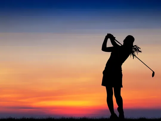 A silhouette of a golfer completing a swing against a colourful sunset sky.