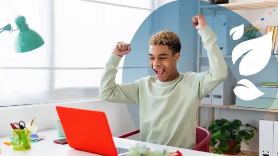 Teen boy celebrating success in front of a red laptop at a tidy home study desk.