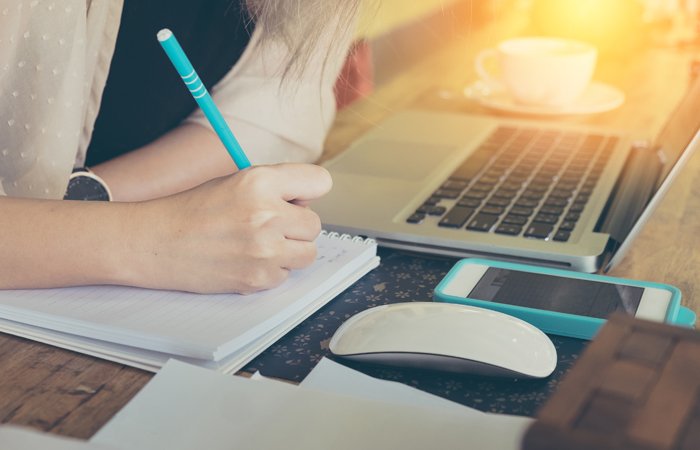 Student engaged in blended learning for online courses, using both a laptop and traditional notes.