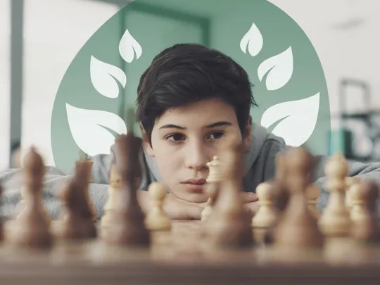 Focused boy resting his head on folded arms, observing a chessboard closely.
