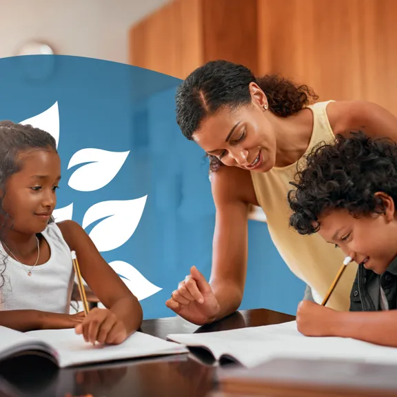 Smiling parent helping two children with their studies at the kitchen table.