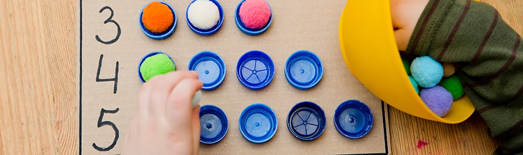 Child sorting colourful pom-poms into numbered bottle tops as part of a hands-on maths activity