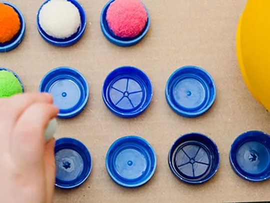 Child sorting colourful pom-poms into numbered bottle tops as part of a hands-on maths activity