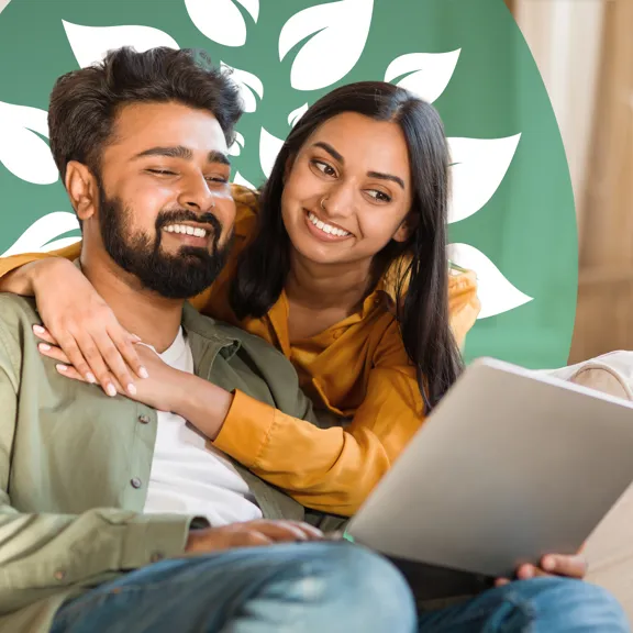 Couple smiling warmly while looking at a laptop together on a cosy living room sofa.