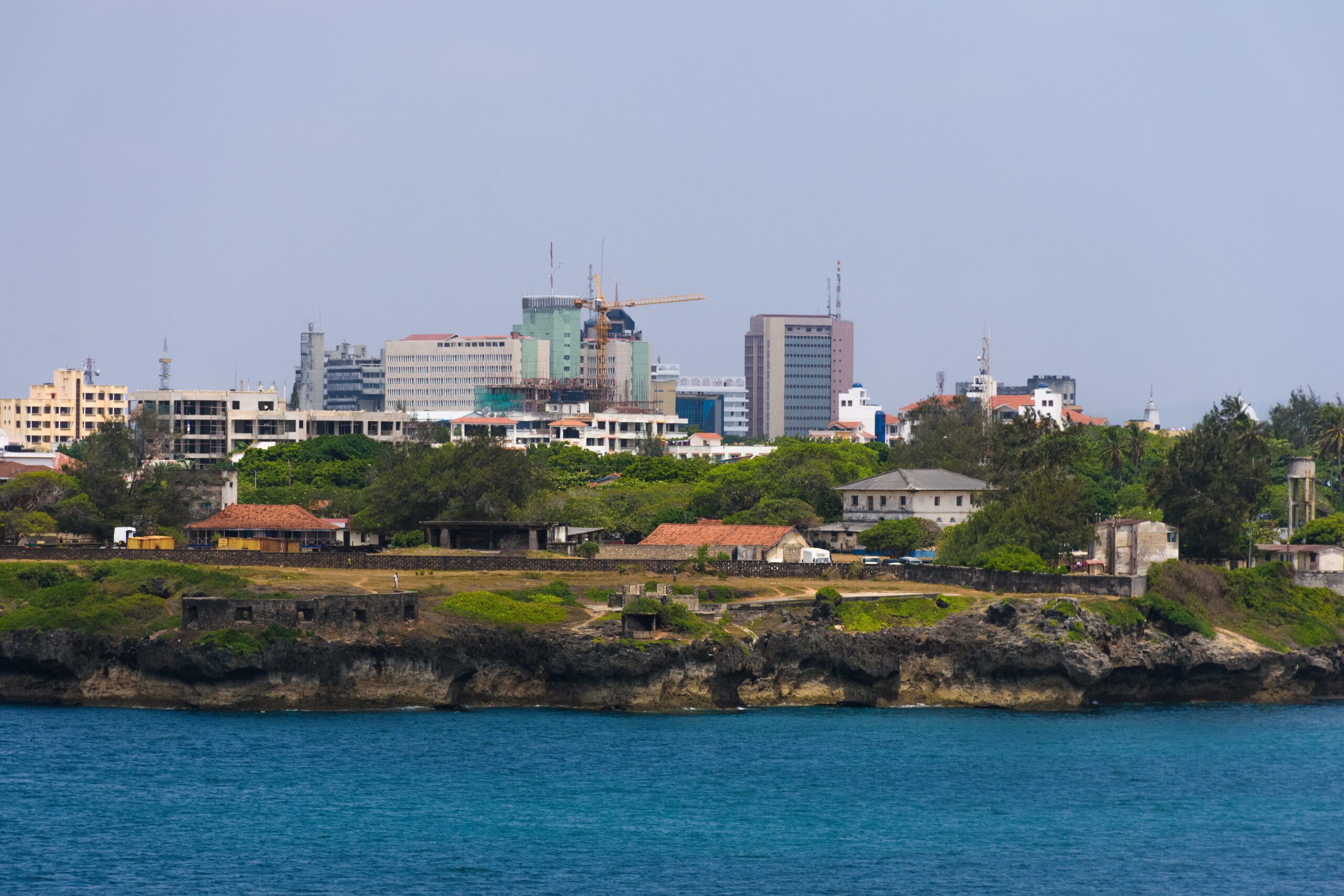 Cityscape of Mombasa viewed from across the water, with modern buildings and coastal vegetation.