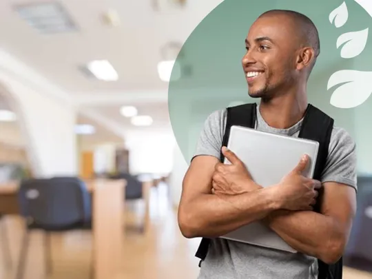 A young man with a black rucksack smiling to the left, holding a laptop to his chest with both arms.