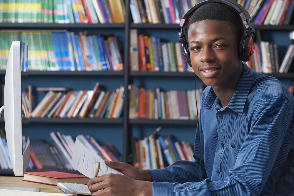 Male GCSE Level student using a computer, and making notes on his studies. 