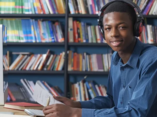Male GCSE Level student using a computer, and making notes on his studies.