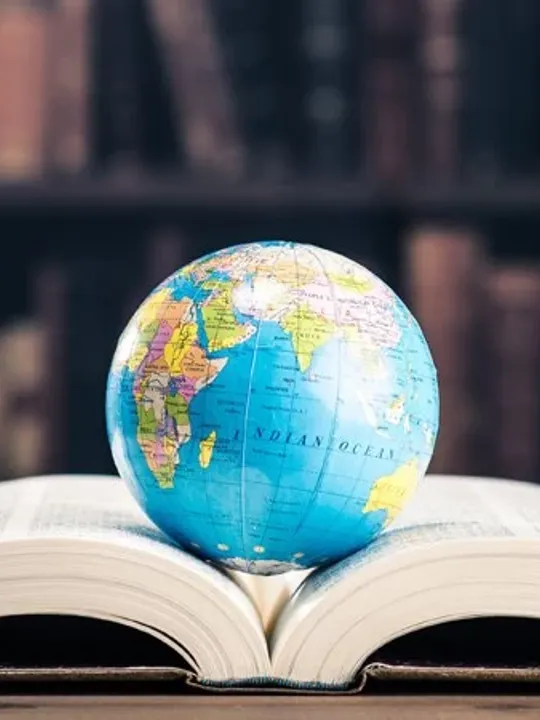 A large book within a library open at the middle with a globe laid on top of it.