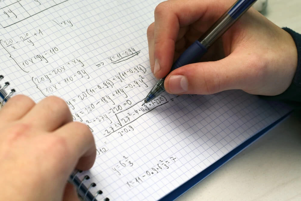 A student completing maths sums in a maths workbook. 