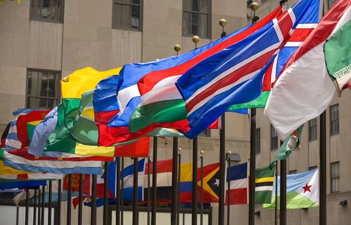 A range of flags from around the world on flagpoles raised at full mast. 