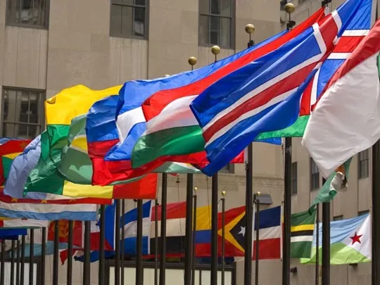 A range of flags from around the world on flagpoles raised at full mast.