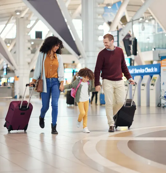 Smiling family travelling together through airport with wheeled suitcases