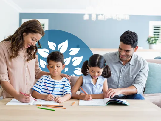 Two parents supporting their young children with schoolwork around a living room table.