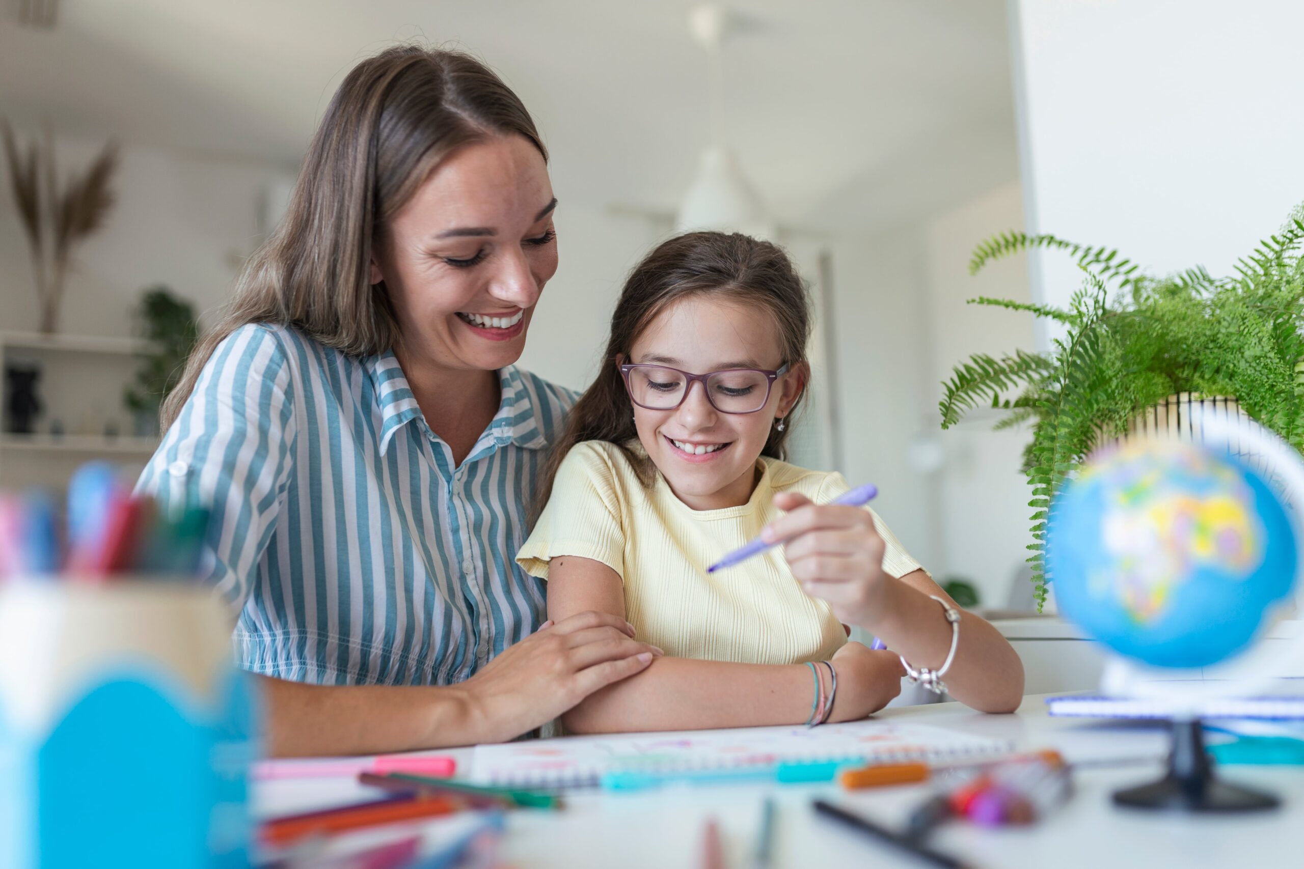 Mom and daughter engaged in a study session at a table, both smiling and looking at educational materials