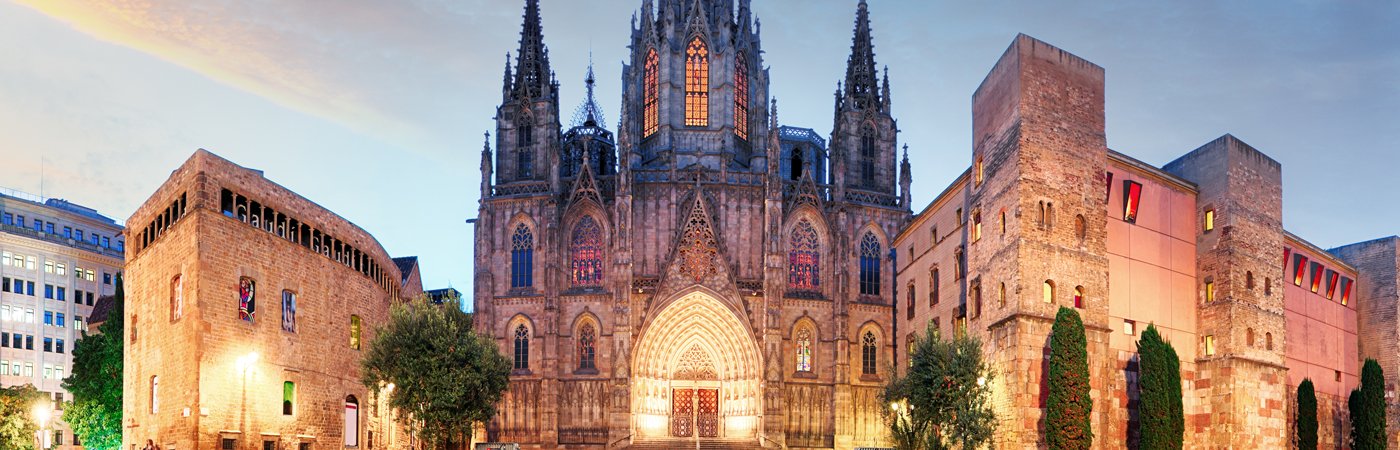 A landscape view of a Spanish church in the early evening, lit up by warm lights. 