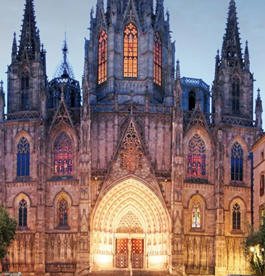 A landscape view of a Spanish church in the early evening, lit up by warm lights.