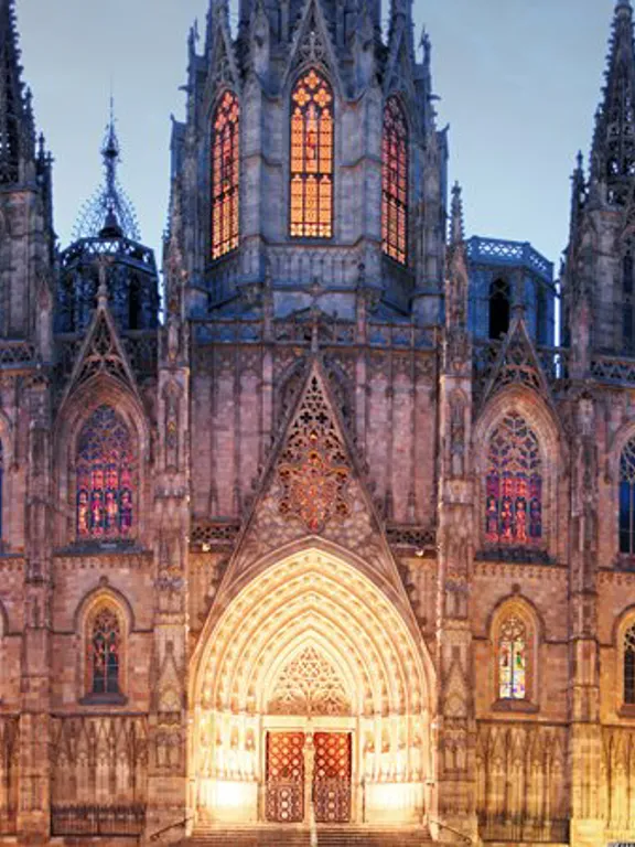 A landscape view of a Spanish church in the early evening, lit up by warm lights.