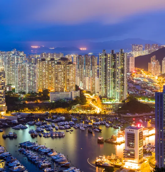 Densely packed high-rise buildings lit at night with a marina full of boats below