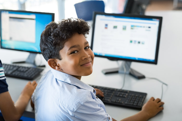 Smiling student using a desktop computer in a classroom setting, engaged in a computing activity