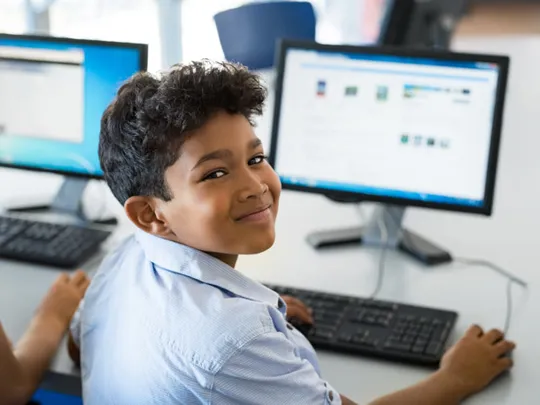 Smiling student using a desktop computer in a classroom setting, engaged in a computing activity