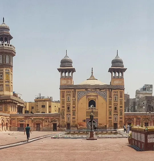 Historic mosque and courtyard in Lahore, Pakistan with people walking through the complex.