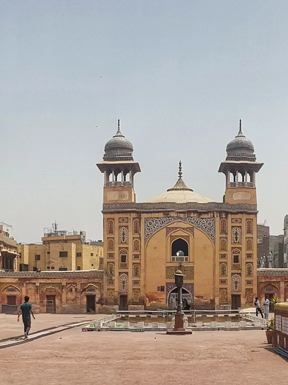 Historic mosque and courtyard in Lahore, Pakistan with people walking through the complex.