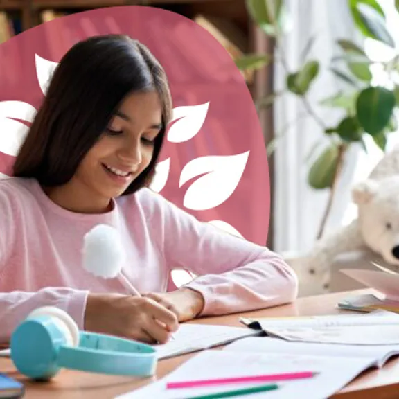 A homeschooling young female student writing in an exercise book at her bedroom desk.