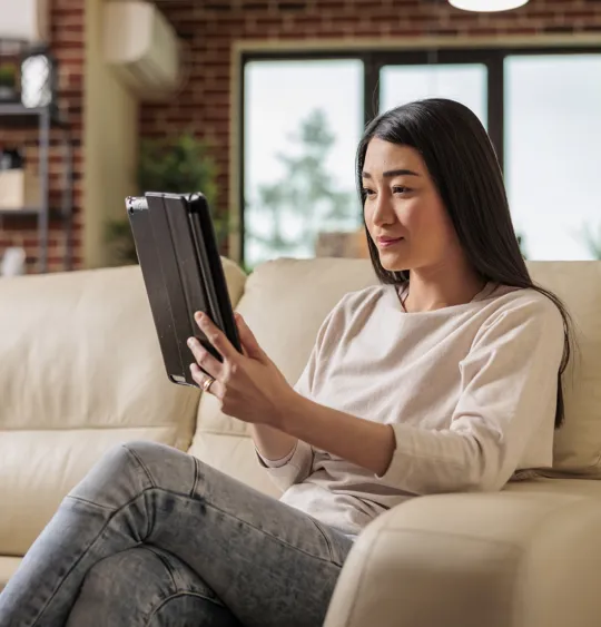 Young woman on cream sofa focused on a tablet in a modern living room setting.