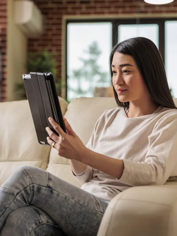 Young woman on cream sofa focused on a tablet in a modern living room setting.